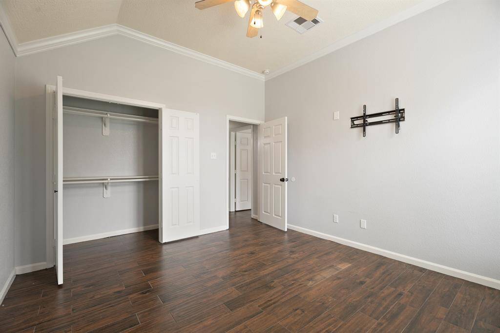 This room features hardwood floors, light gray walls, and a ceiling fan. It includes a spacious closet with double doors and a wall mount for a TV.
