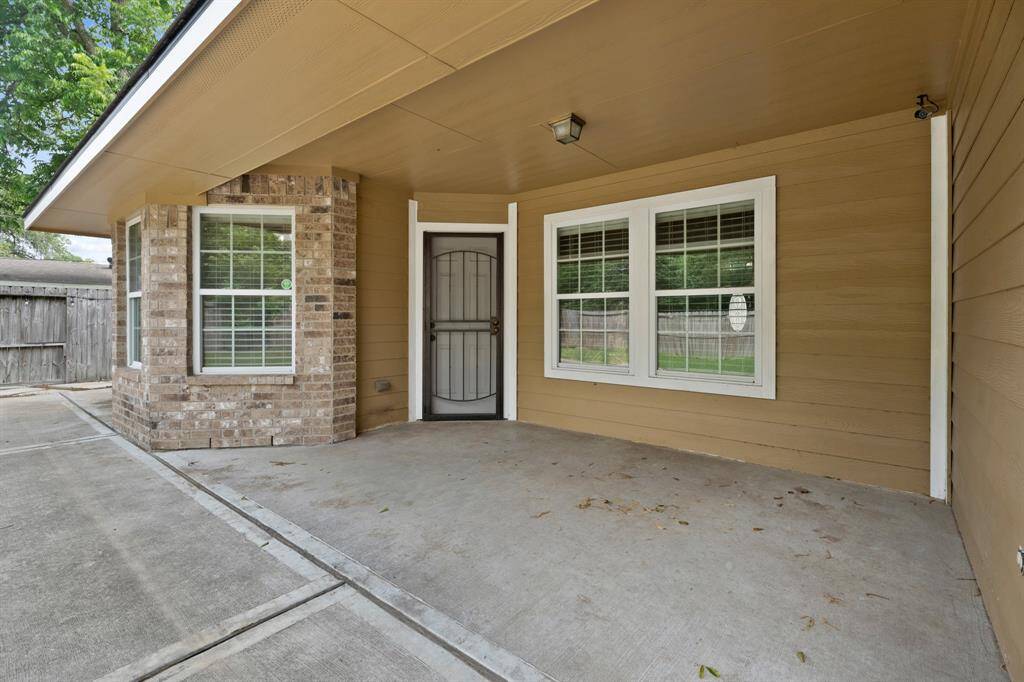 This photo shows a covered front porch with a concrete floor, brick and siding exterior, and two large windows. It features a secure front door and is adjacent to a driveway, offering a welcoming entrance with ample space.