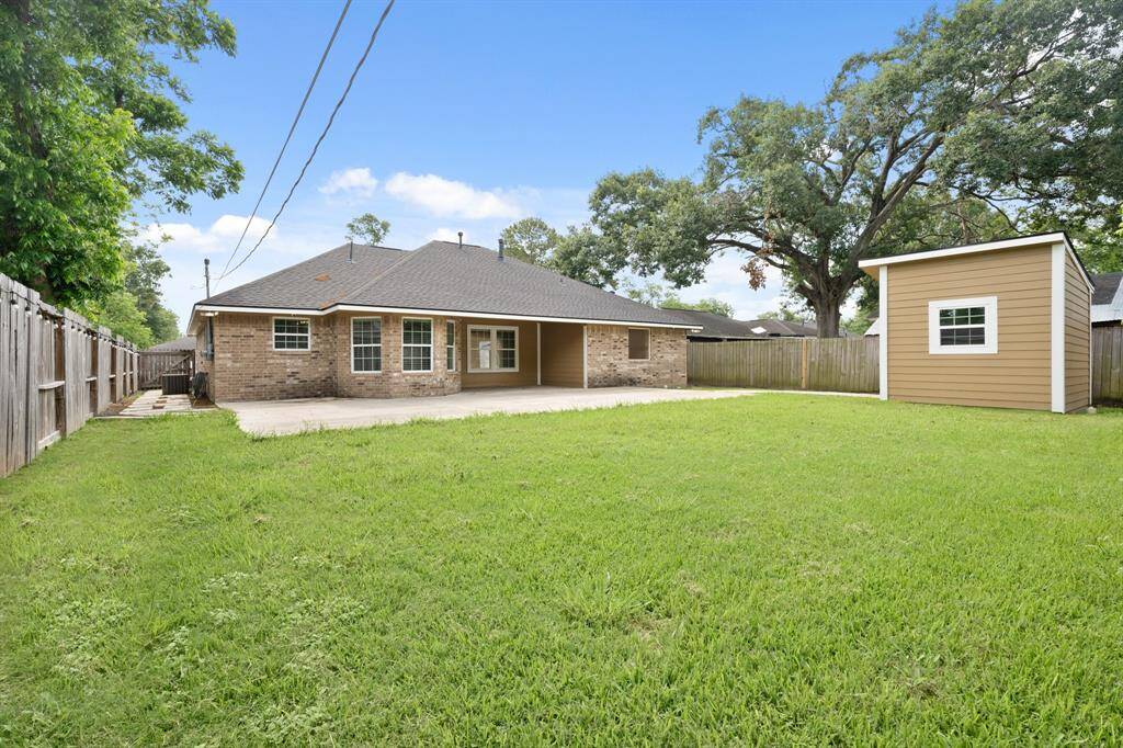 This photo showcases a spacious backyard with a well-maintained lawn, a brick house with a covered patio area, and a separate storage shed. The yard is fully fenced, offering privacy and ample outdoor space.