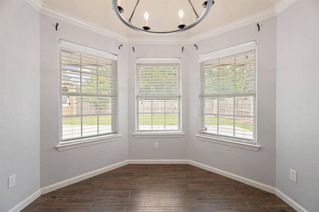 Bright and inviting space with large windows, offering a view of the backyard. The room features wood-style flooring and a modern chandelier, perfect for a cozy dining area or breakfast nook.