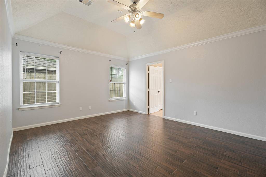 This spacious, bright room features two large windows, wood-look flooring, and a ceiling fan. The neutral walls and crown molding add a touch of elegance, with a door leading to another area of the home.