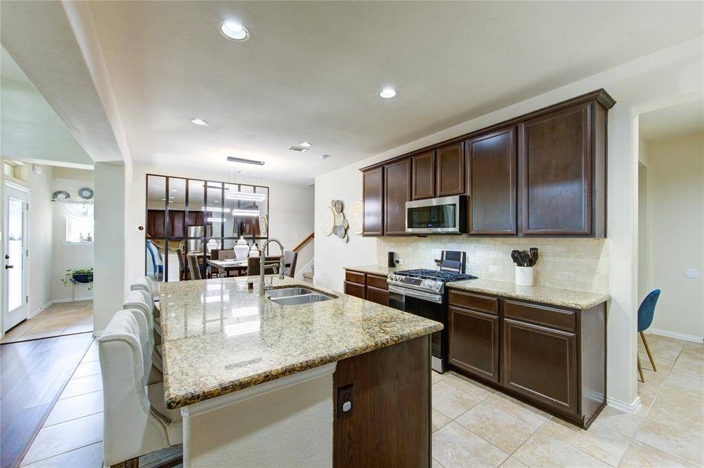 This modern kitchen features granite countertops, dark wood cabinets, and stainless steel appliances. The open layout connects to the dining area, creating a spacious and inviting atmosphere. Natural light enhances the bright, airy feel.