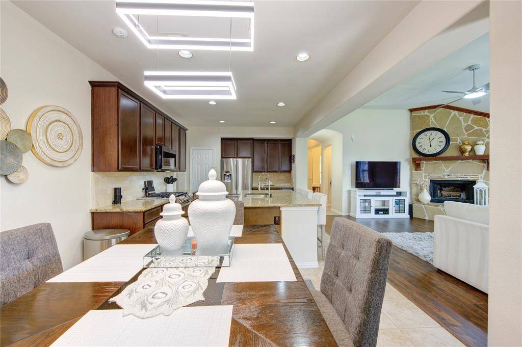 This photo showcases a modern open-concept kitchen and living area. The kitchen features dark wood cabinets, stainless steel appliances, and a central island. The adjacent living space includes a stone fireplace, large clock, and built-in shelving, creating a cozy yet stylish atmosphere.
