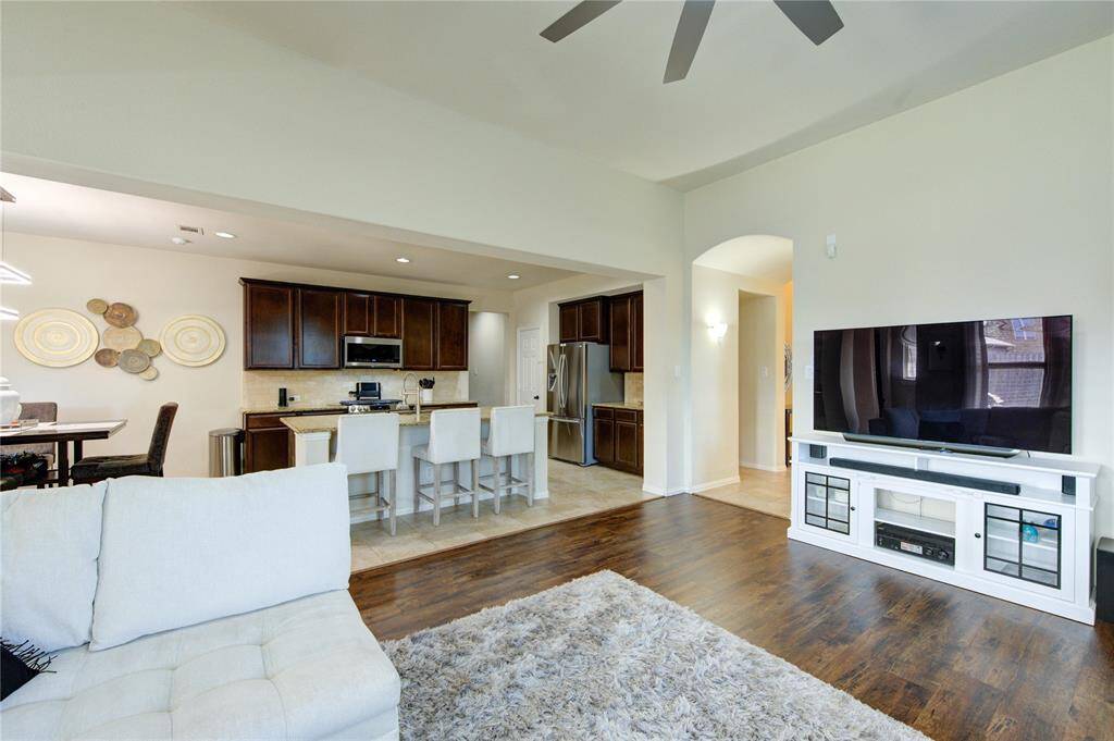 This photo showcases an open-concept living area with wood flooring, featuring a modern kitchen with dark cabinetry and a breakfast bar. The space includes a cozy seating area with a large TV and natural light. Perfect for entertaining and relaxing.