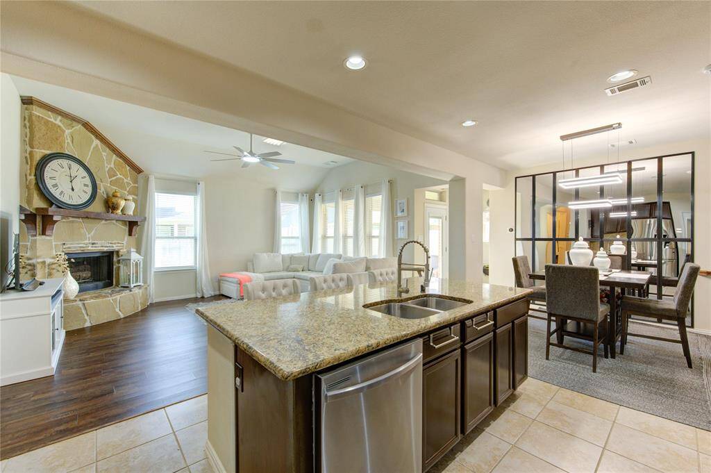 This open-concept living space features a modern kitchen with granite countertops and a central island, flowing into a cozy living room with a stone fireplace and large windows. The adjacent dining area is stylishly separated by a glass partition, enhancing the contemporary feel.