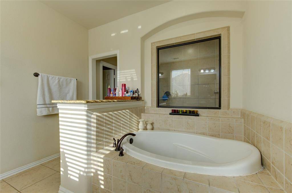 This bathroom features a cozy, tiled bathtub area with a window for natural light, a granite-topped ledge for toiletries, and a neutral color palette for a serene atmosphere.