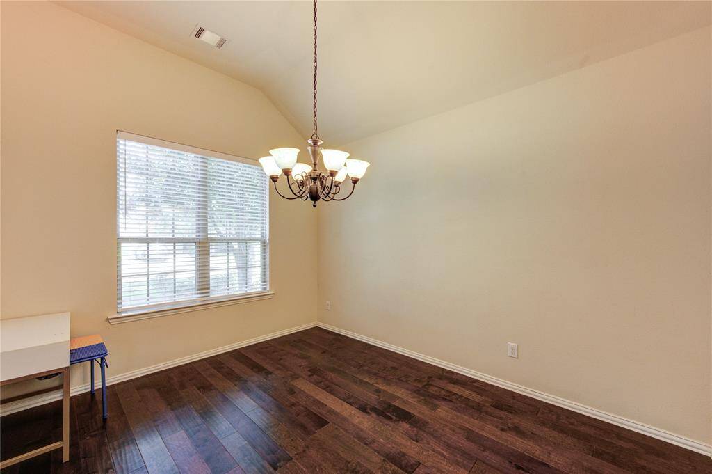 This room features high ceilings and dark hardwood floors, complemented by a large window allowing natural light and an elegant chandelier for additional lighting. Perfect for a dining or living area.