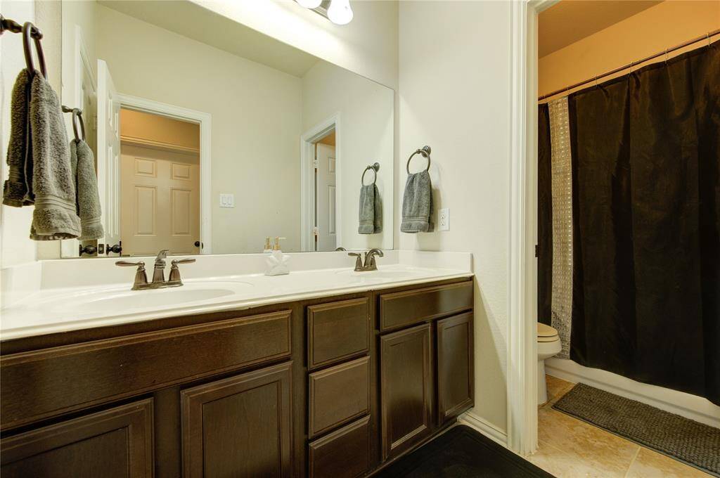 This bathroom features a dual-sink vanity with dark wood cabinets, a large mirror, and a shower area with a dark curtain. Neutral tiles and walls create a clean and modern look.