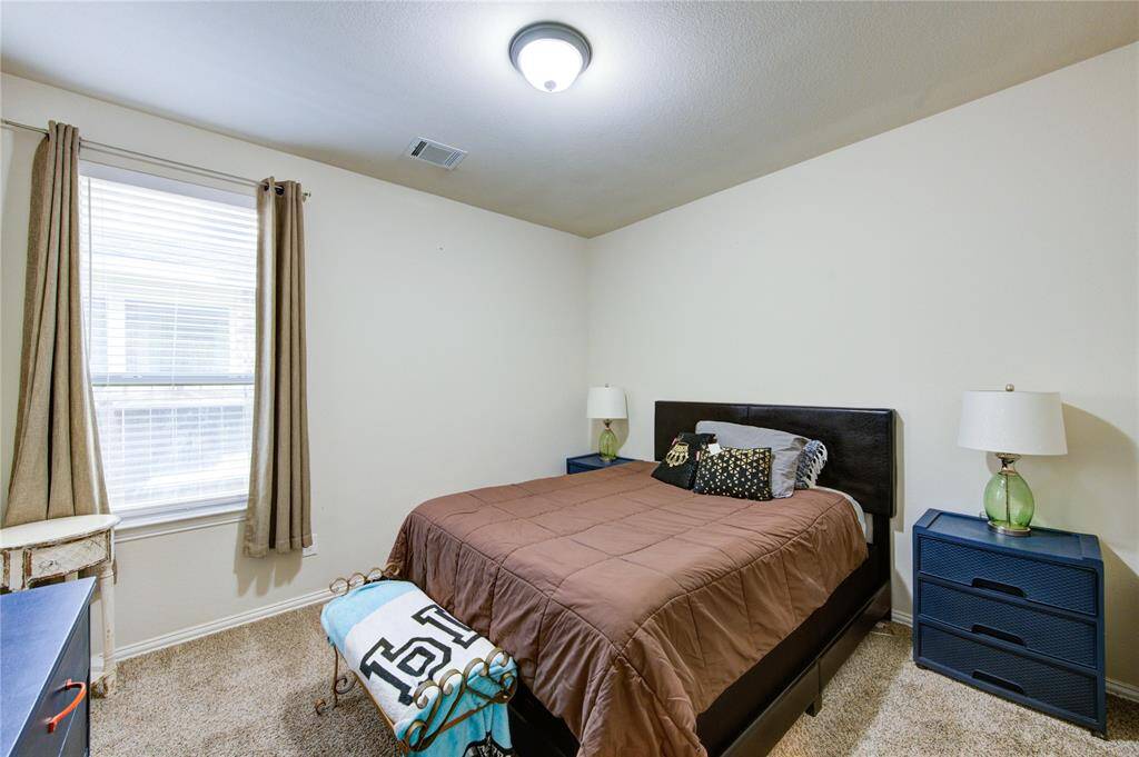 Cozy bedroom featuring a plush bed with brown bedding, two blue nightstands with modern lamps, and a window allowing natural light. Neutral walls and carpet create a warm, inviting atmosphere.