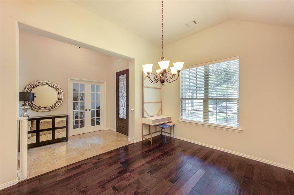 This inviting space features a blend of tiled and dark wood flooring, a large window for natural light, and a stylish chandelier. French doors and a decorative mirror add elegance, while a small desk area offers functionality.