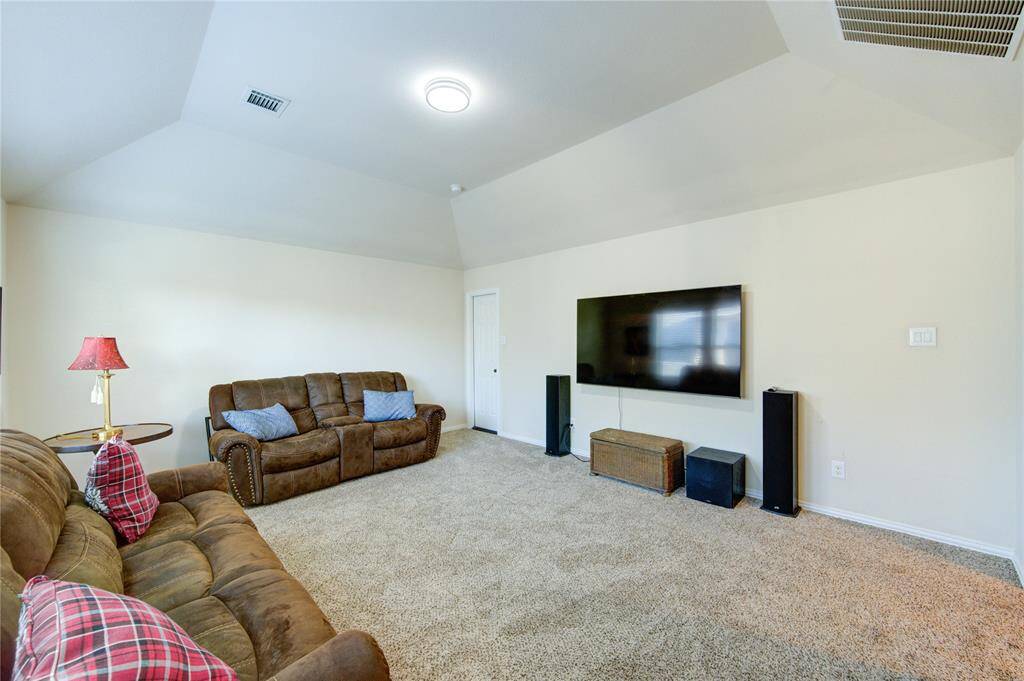 This spacious living room features plush carpeting, a large wall-mounted TV, and comfortable seating, perfect for relaxation and entertainment.