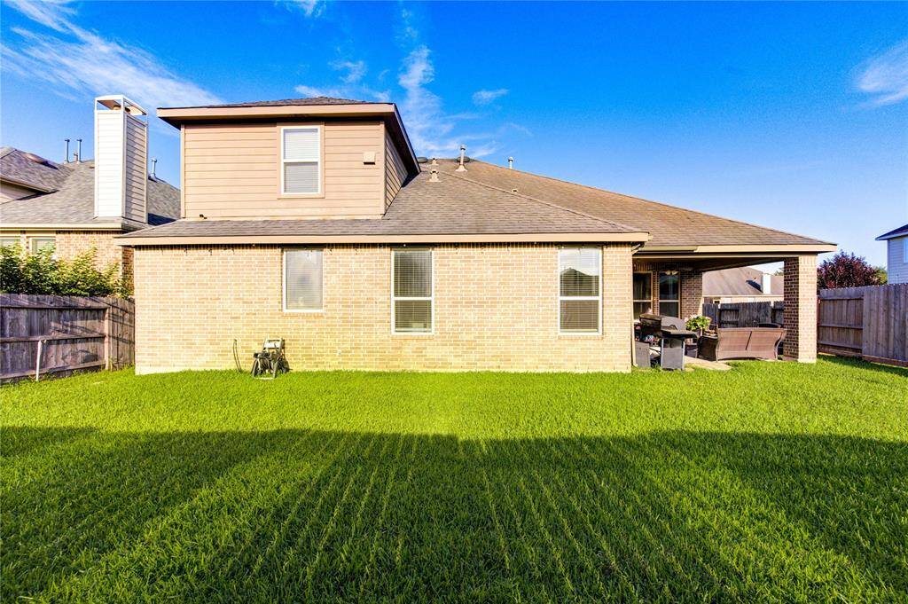 This photo showcases a well-maintained backyard with a lush green lawn, a brick exterior, and a covered patio area perfect for outdoor seating. The house has a two-story section, and there are privacy fences on both sides.