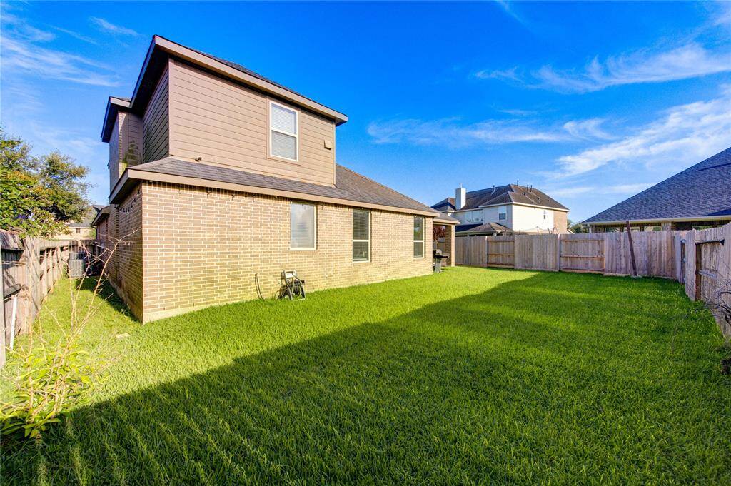This photo shows a two-story brick house with a spacious, well-maintained backyard, enclosed by a wooden fence. It's perfect for outdoor activities and offers privacy.
