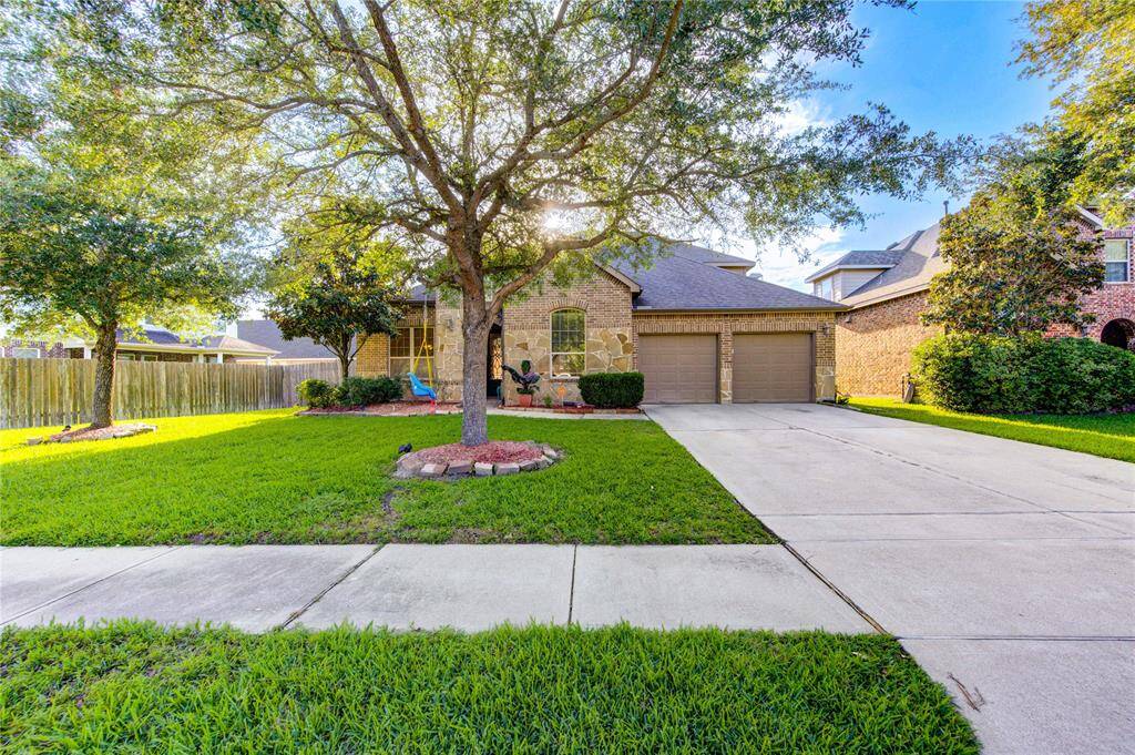 Charming single-story home with a two-car garage, nestled in a well-maintained yard with mature trees and lush greenery. The exterior features a mix of brick and stone, offering great curb appeal in a quiet neighborhood.