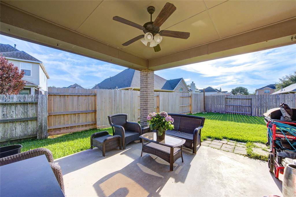 This photo showcases a cozy covered patio with comfortable seating, a ceiling fan, and a view of a fenced backyard. It's perfect for outdoor relaxation and entertaining.