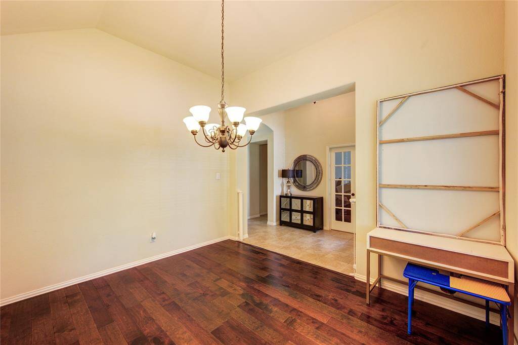 This room features high ceilings and hardwood floors, creating a spacious feel. A chandelier adds elegance, while an open doorway leads to a tiled area with a decorative mirror and console, offering a welcoming transition between spaces.