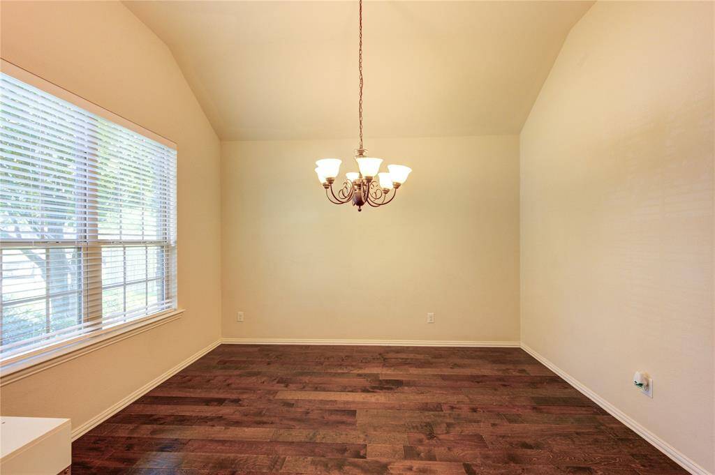 This room features hardwood floors, a large window with blinds for natural light, and a central chandelier, ideal for dining or as a flex space.