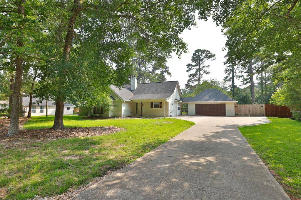 Charming single-story home with a spacious driveway leading to a two-car garage. The house is surrounded by lush trees, offering a serene and private setting. A large front lawn enhances its curb appeal.