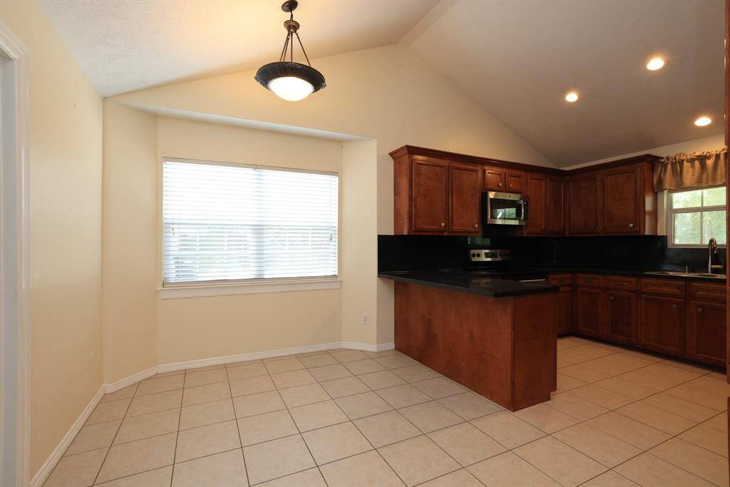 Spacious kitchen with rich cabinetry, ample counter space, and modern appliances. It features a vaulted ceiling, tile flooring, and a large window for natural light.