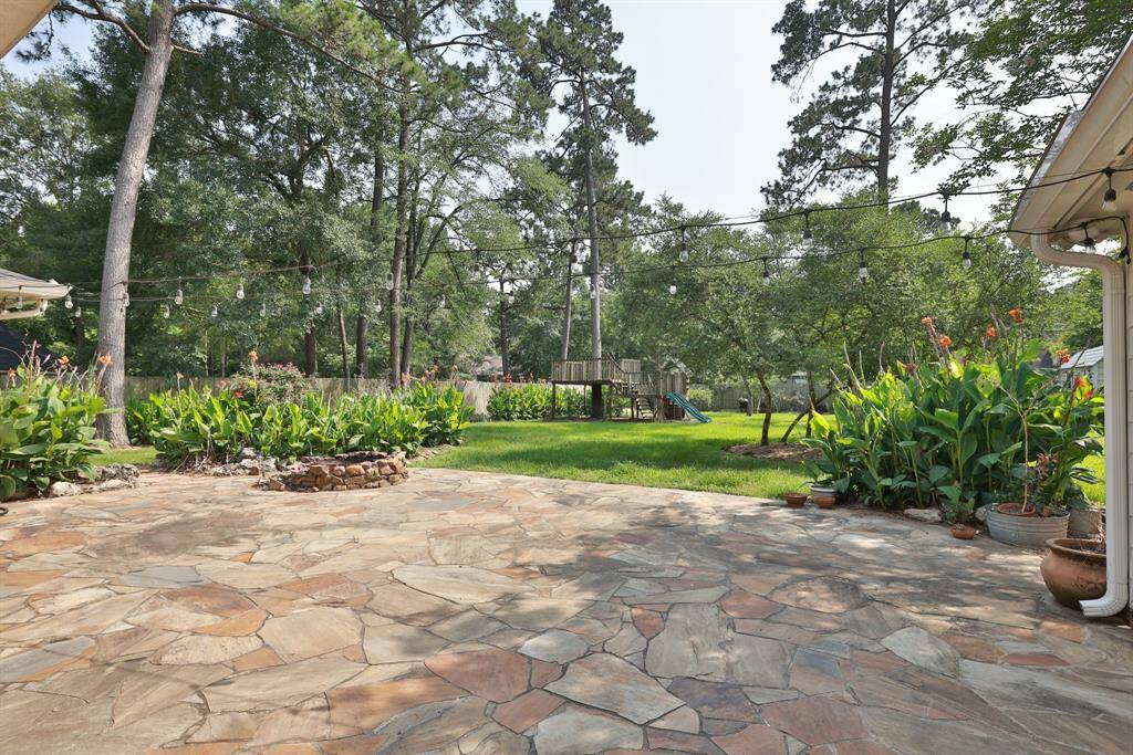 This photo showcases a charming backyard with a spacious stone patio, ideal for outdoor entertaining. The home features light siding, and lush lanscape. French doors offer easy access to the patio, enhancing indoor-outdoor living.