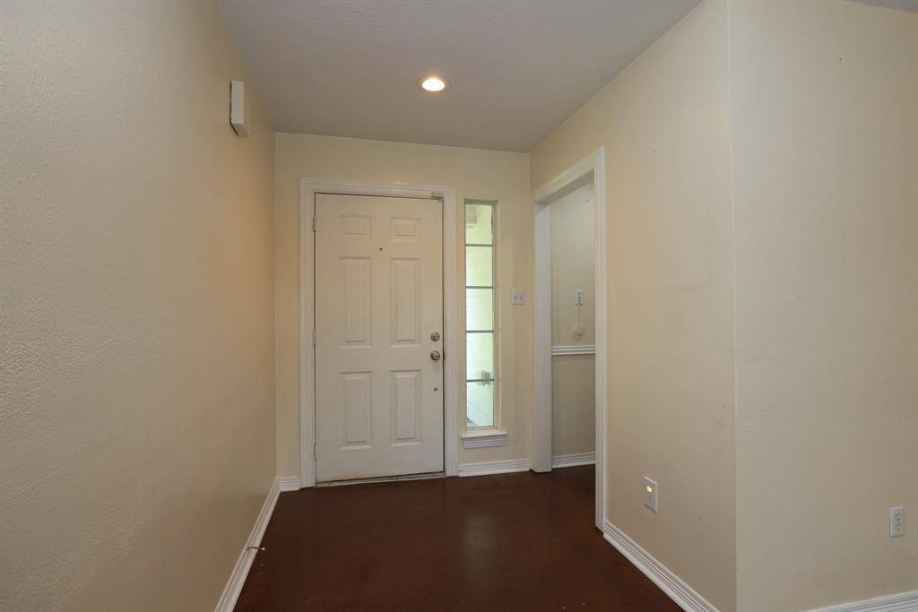 This photo shows a functional entryway with a white front door and a transom side window for natural light. The walls are painted a neutral color, and the space features recessed lighting.
