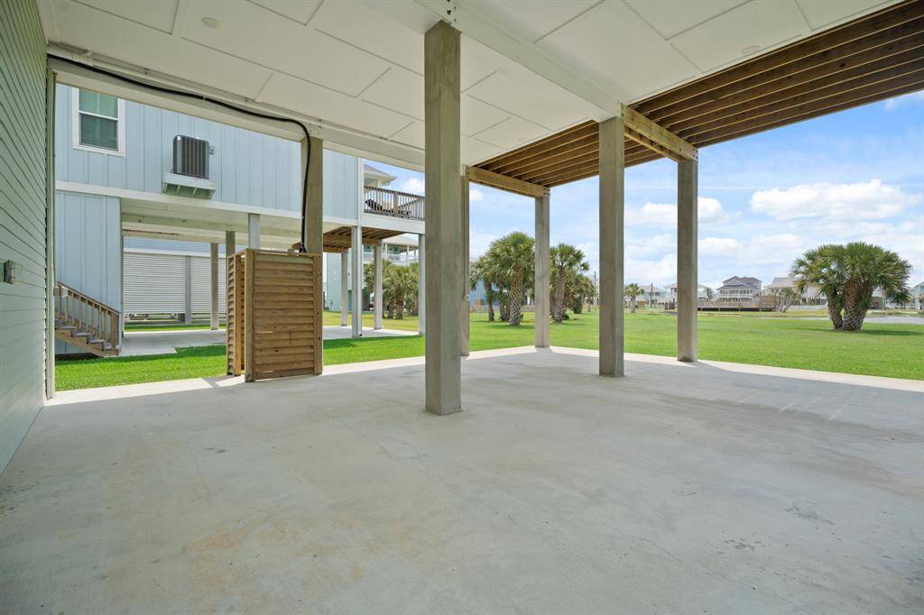 Ground level view of entertainment space behind the garage, outdoor shower, back yard and concrete support beams
