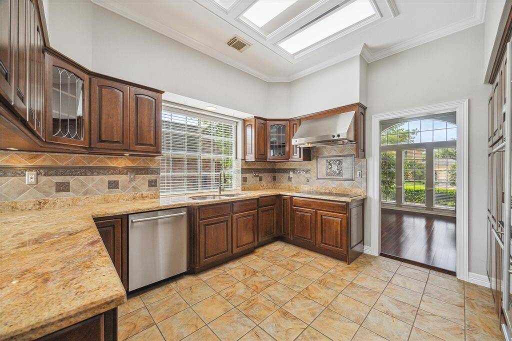 The kitchen shines with rich wood cabinetry, granite countertops, and a custom tile backsplash with detailed accents above the range.