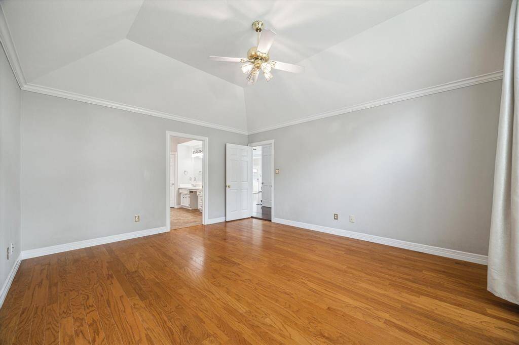 The spacious primary bedroom features a dramatic vaulted ceiling and rich hardwood flooring, creating a serene and elegant retreat.