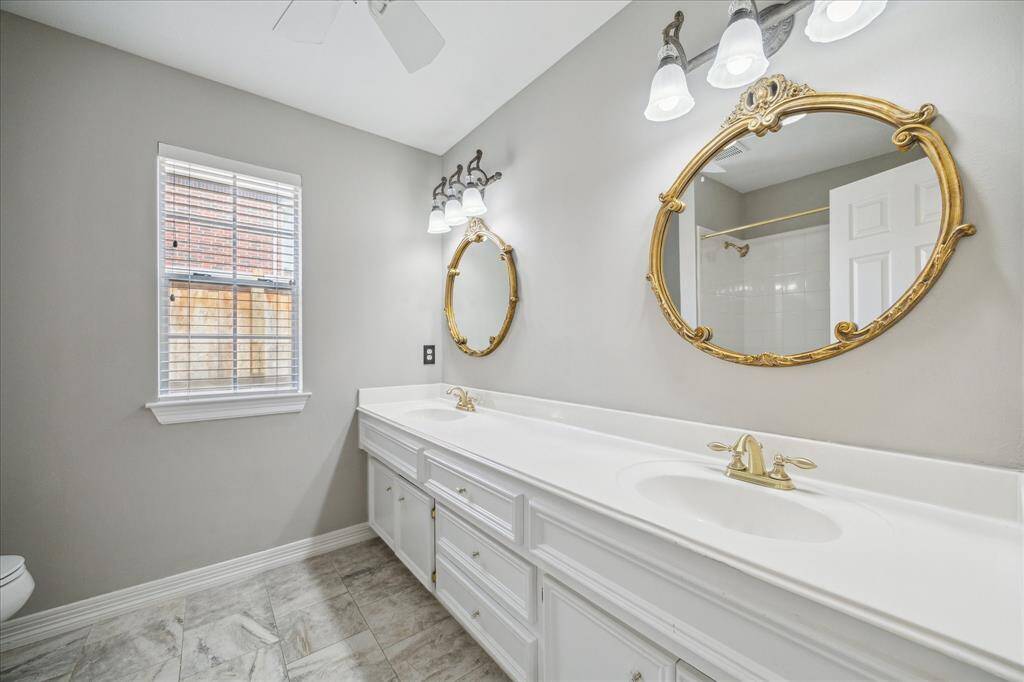 The shared secondary bathroom is both stylish and functional, featuring a long dual-sink vanity with vintage-inspired gold mirrors and updated lighting.