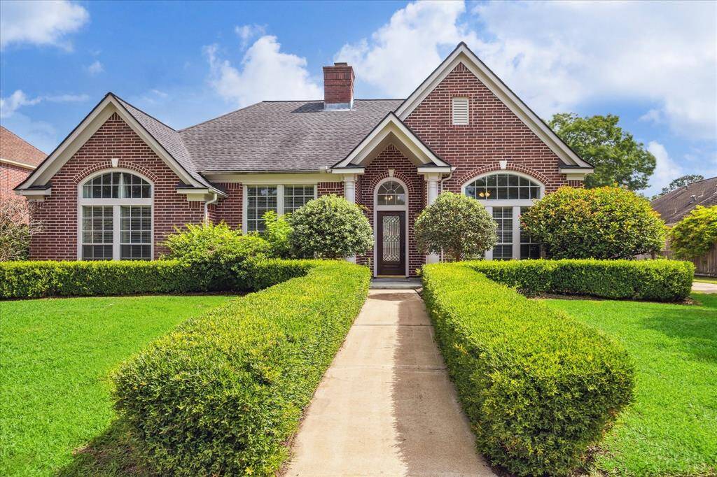 A welcoming front walkway bordered by pristine hedges draws you to the inviting brick entry, framed by elegant columns and arched windows.