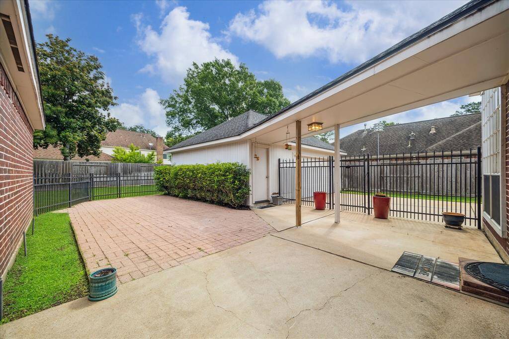 A covered breezeway connects the garage and home, leading to a paved patio perfect for outdoor seating.
