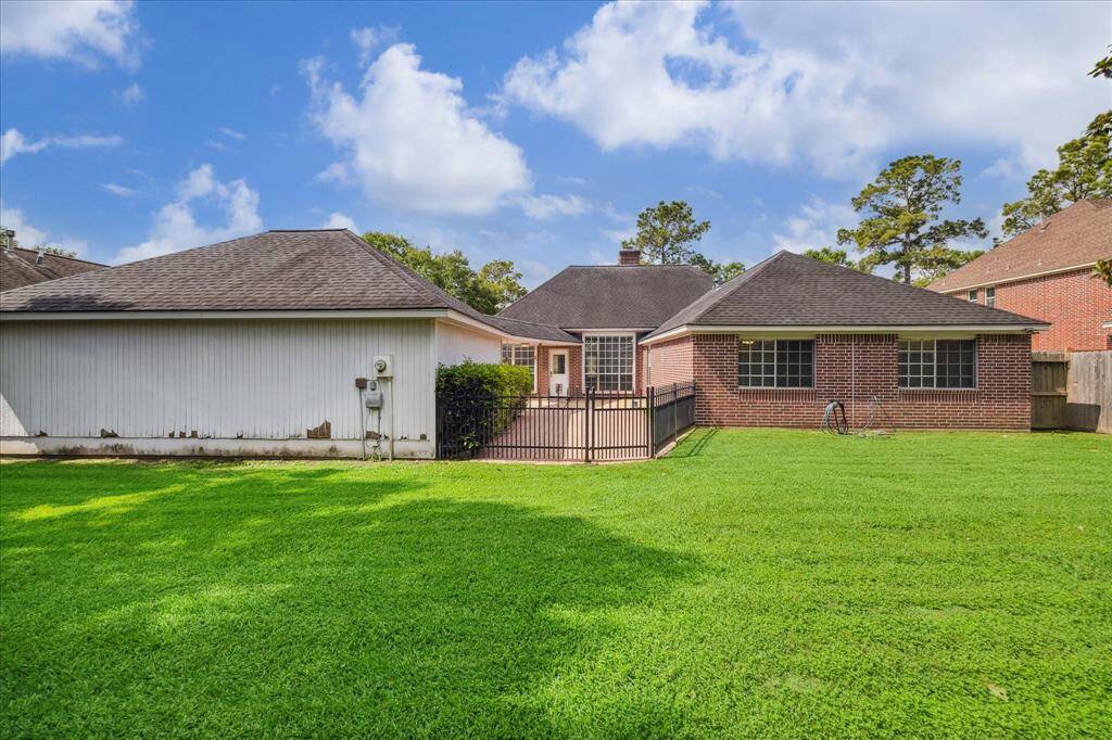 The fully fenced backyard features a wrought-iron gate separating the green space from the patio area.
