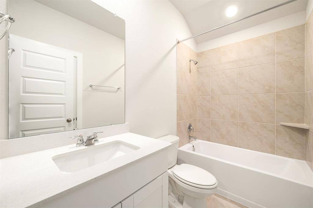 This secondary bathroom features a clean, modern design with soft neutral tones. A sleek vanity with a quartz countertop pairs seamlessly with the large mirror, while the tiled shower and tub combination offers a practical and stylish bathing space. Bright lighting and a minimalist layout complete the fresh, contemporary look.
