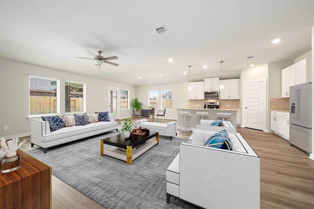 Bright and open, this stunning living area features large windows that fill the space with natural light, a seamless flow into the modern kitchen with white cabinetry, granite countertops, and stainless steel appliances. The expansive layout offers plenty of room for entertaining and everyday living, all set on stylish wood-look flooring.