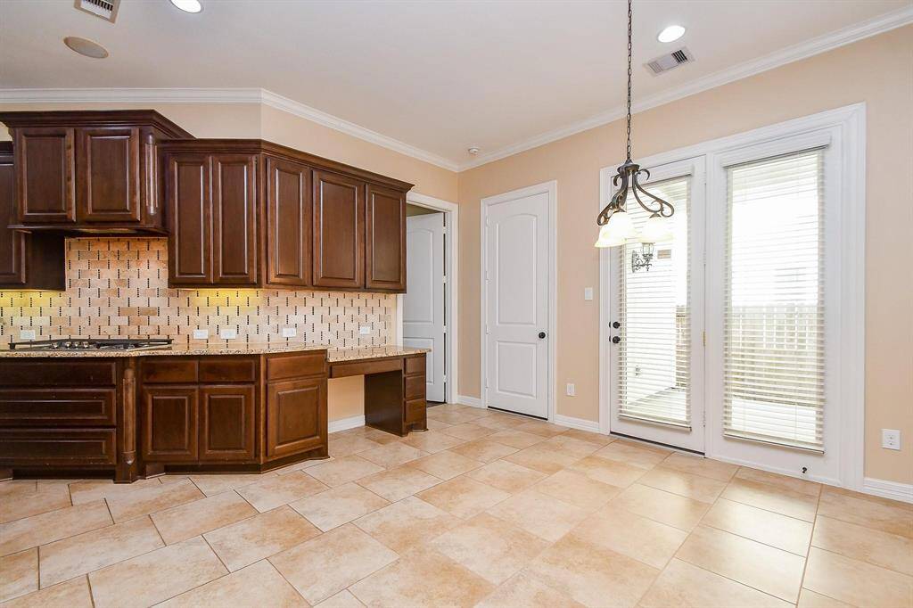 This open-concept living space features a spacious layout with tile flooring, a cozy stone fireplace, and a ceiling fan. The kitchen boasts a large island, dark wood cabinetry, and modern lighting. A staircase leads to the upper level, adding to the home's elegant design.