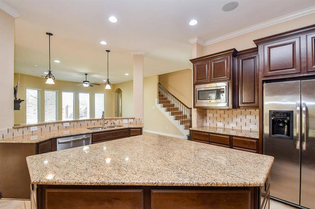 Spacious living room with large tiled floors and neutral walls, featuring a stone fireplace and built-in TV. The room is brightened by multiple tall windows and a ceiling fan, offering a modern and inviting atmosphere.
