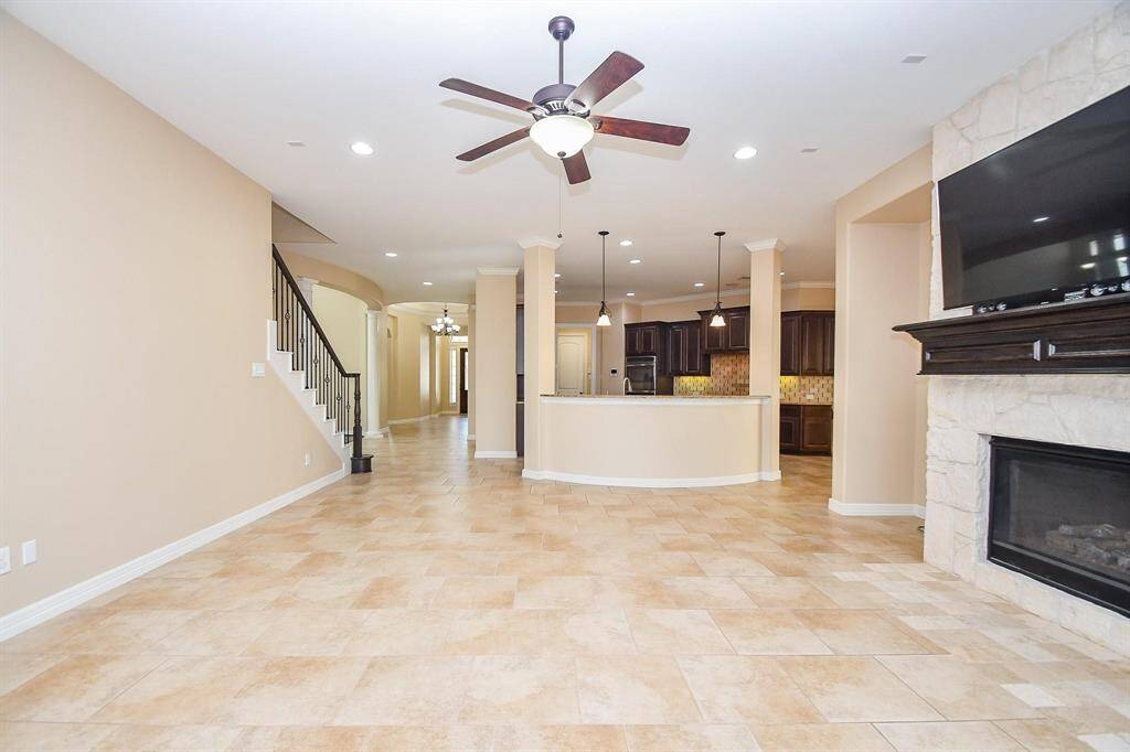 This spacious  Master bedroom features light wood flooring and neutral walls with crown molding. It includes a tray ceiling with recessed lighting, a ceiling fan, and a large window for natural light. French doors lead to an adjoining room, possibly a bathroom.