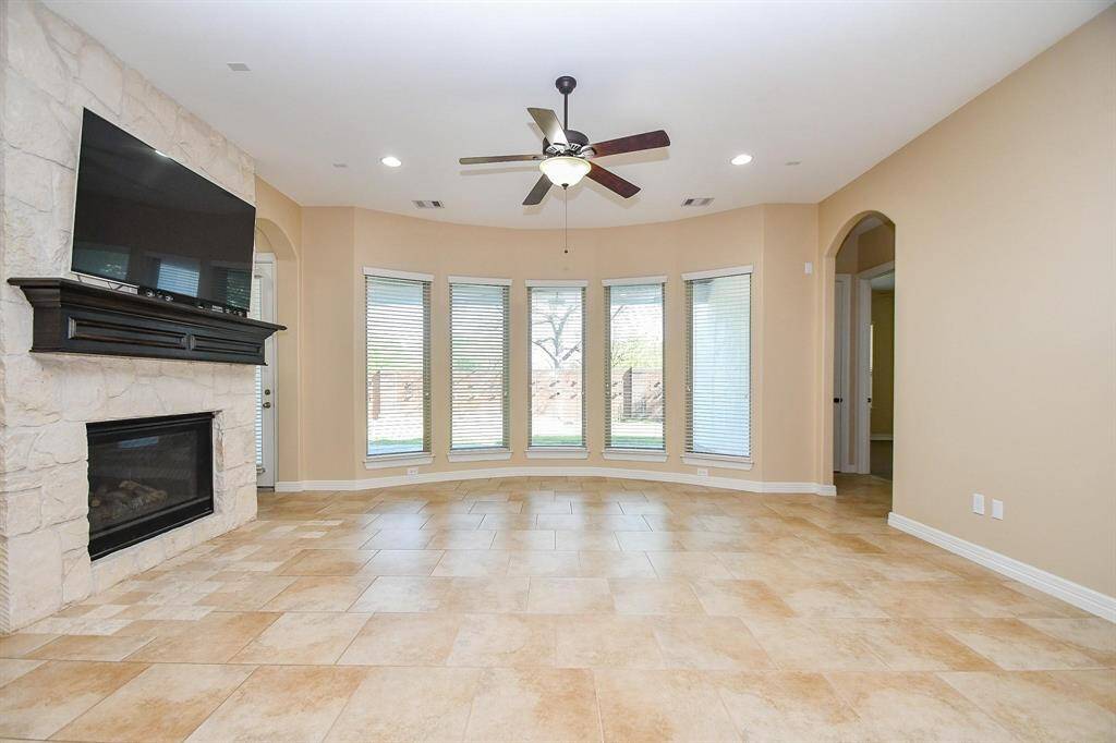 This spacious bedroom features a tray ceiling with recessed lighting and a ceiling fan, light wood flooring, and neutral walls. Double doors open to an en-suite bathroom with a large tub and double vanity.