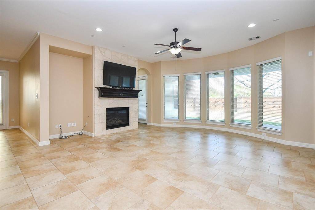 Spacious room with light wood flooring and neutral walls, featuring a tray ceiling with a ceiling fan. Large windows provide ample natural light, creating a bright and inviting atmosphere.