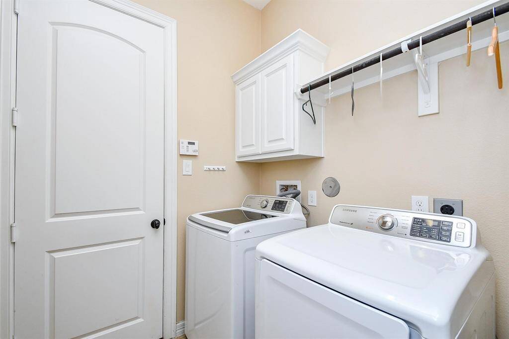 This is a bright, well-organized laundry room featuring a washer and dryer, storage cabinet, hanging rod, and a neutral color palette.