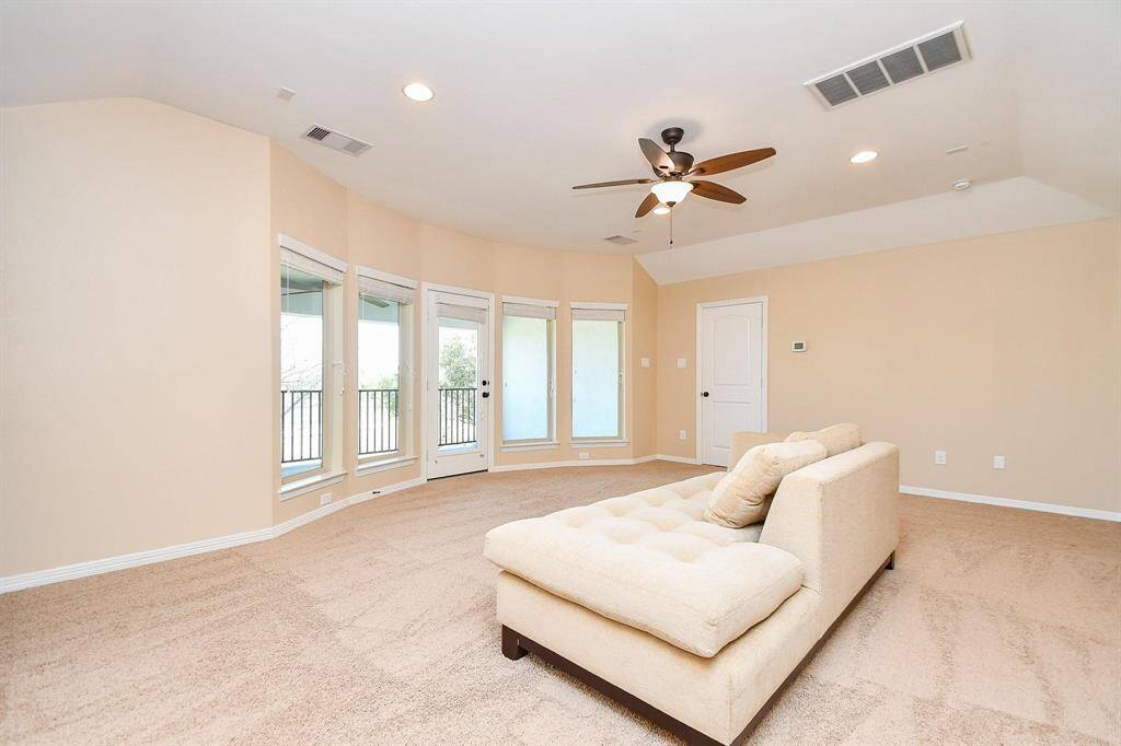 This spacious Game room features neutral walls and carpet, a ceiling fan, and abundant natural light from multiple windows and a glass door leading to a balcony, offering a cozy and inviting atmosphere.