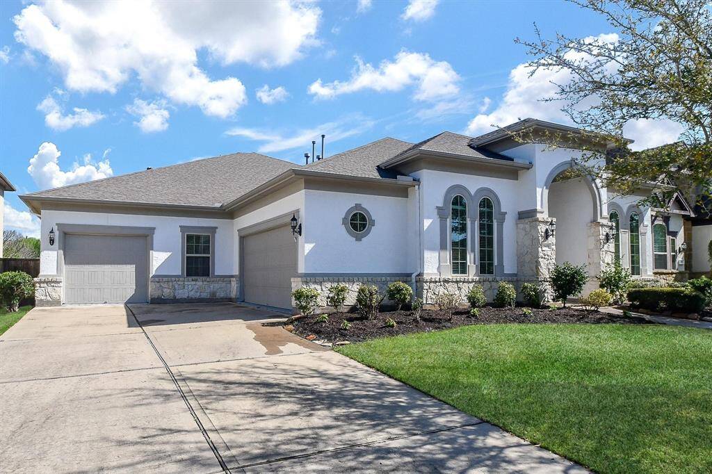 This is a modern, single-story home with a clean white exterior, stone accents, and arched windows. It features a double garage, a well-maintained lawn, and a spacious driveway. Perfect for those seeking a blend of style and functionality.