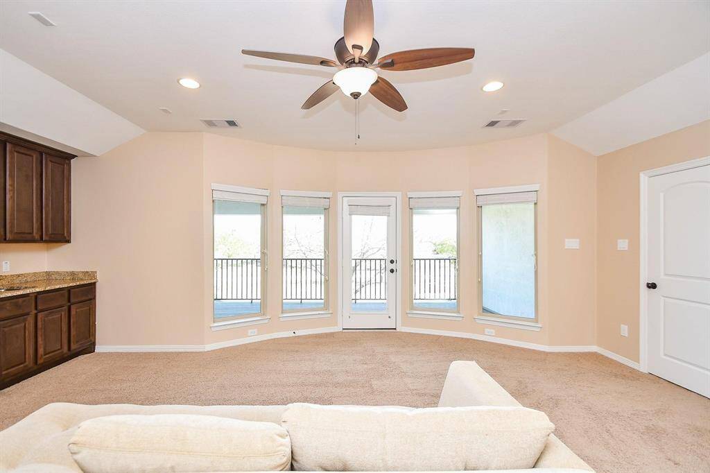 This bright living space features a ceiling fan, recessed lighting, and a cozy carpeted floor. Large windows and a glass door lead to a balcony, offering plenty of natural light and views. The room includes built-in dark wood cabinetry with granite countertops.