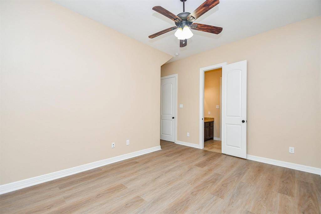 Bright bedroom with neutral walls and wood flooring. Features a ceiling fan, double doors, and an en-suite bathroom.
