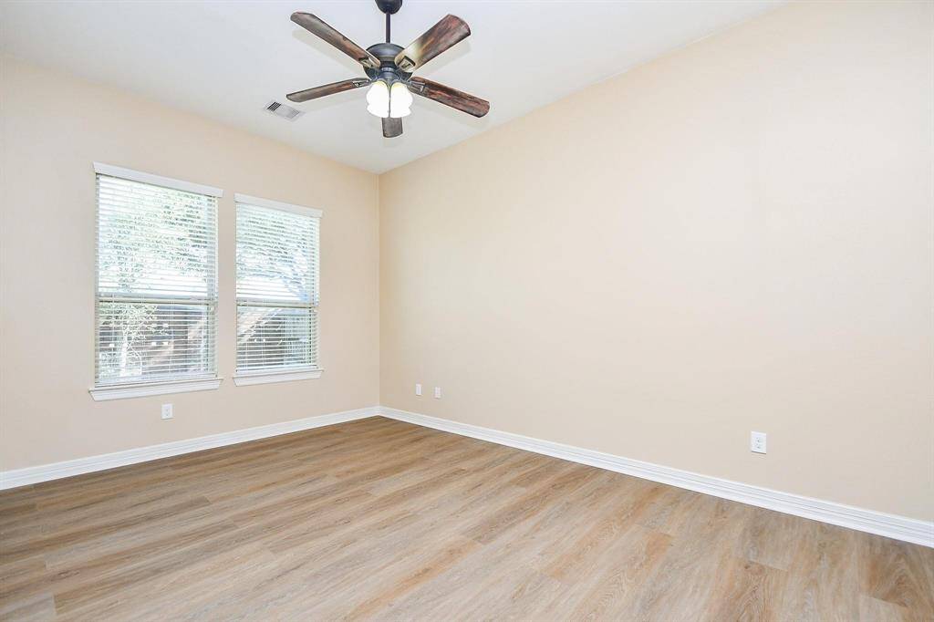This room features neutral walls, wood-look flooring, and two large windows for natural light. It includes a ceiling fan, creating a comfortable and airy space.
