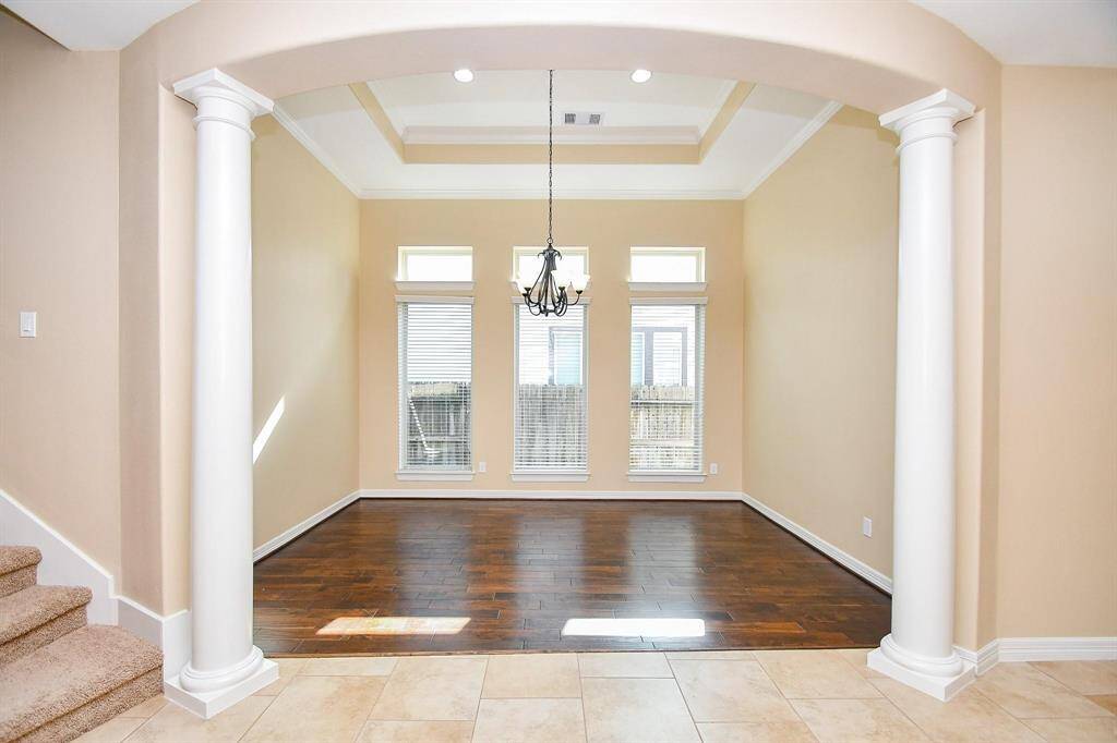 This elegant  Dining room features high ceilings with a tray design, large windows for natural light, hardwood floors, and a central chandelier. The space is framed by classic white columns, creating an open and inviting atmosphere.