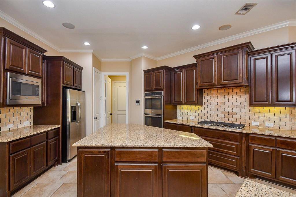 This spacious home features an elegant entryway with a chandelier, tiled floors, and a curved staircase. The open-concept kitchen offers dark wood cabinets, a breakfast bar, and stylish pendant lighting, creating a warm and inviting atmosphere.