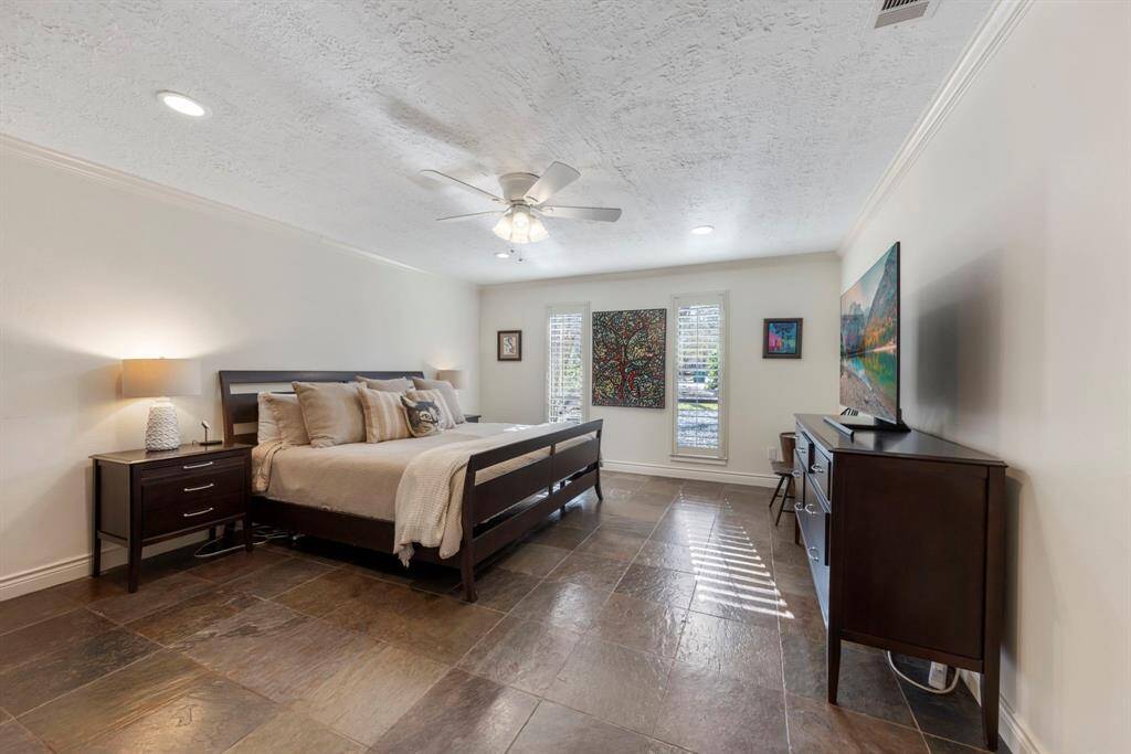 The downstairs private primary suite features tile flooring, crown molding, plantation shuttered windows, and a ceiling fan, creating a serene and comfortable retreat.