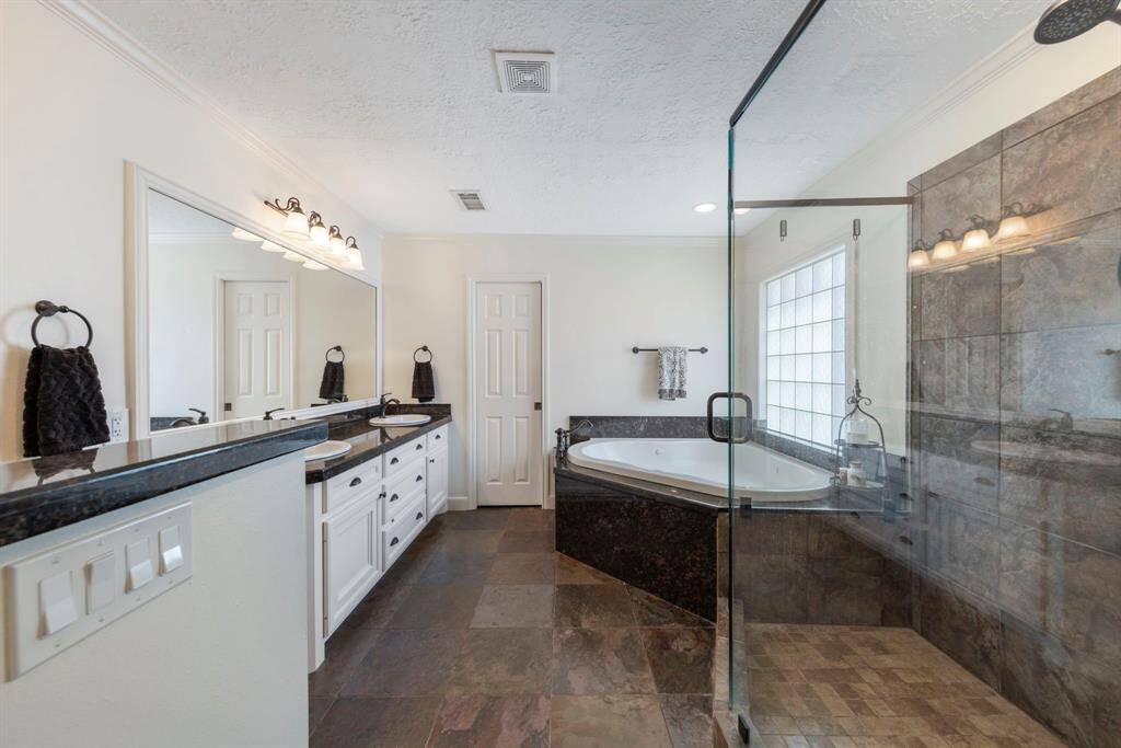 The private primary bathroom boasts tile flooring, an oversized tile shower, a large jetted tub, dual sinks with granite countertops, and a spacious walk-in closet.