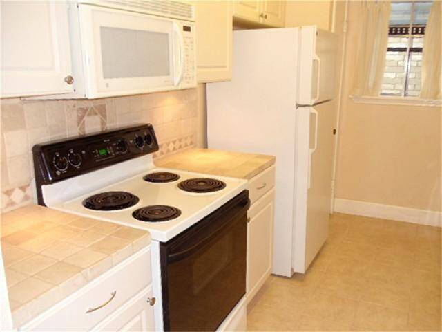 Galley kitchen with tile countertops, space-saver microwave and great window for natural light!